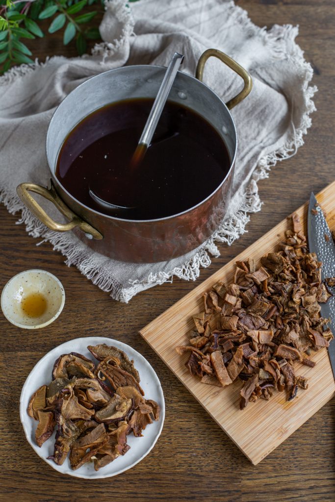 Mushroom stock in a pot, sliced mushrooms on a cutting board.