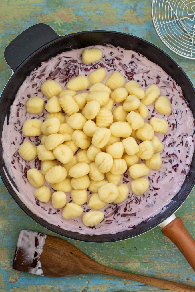 Adding cooked gnocchi to radicchio cream sauce.