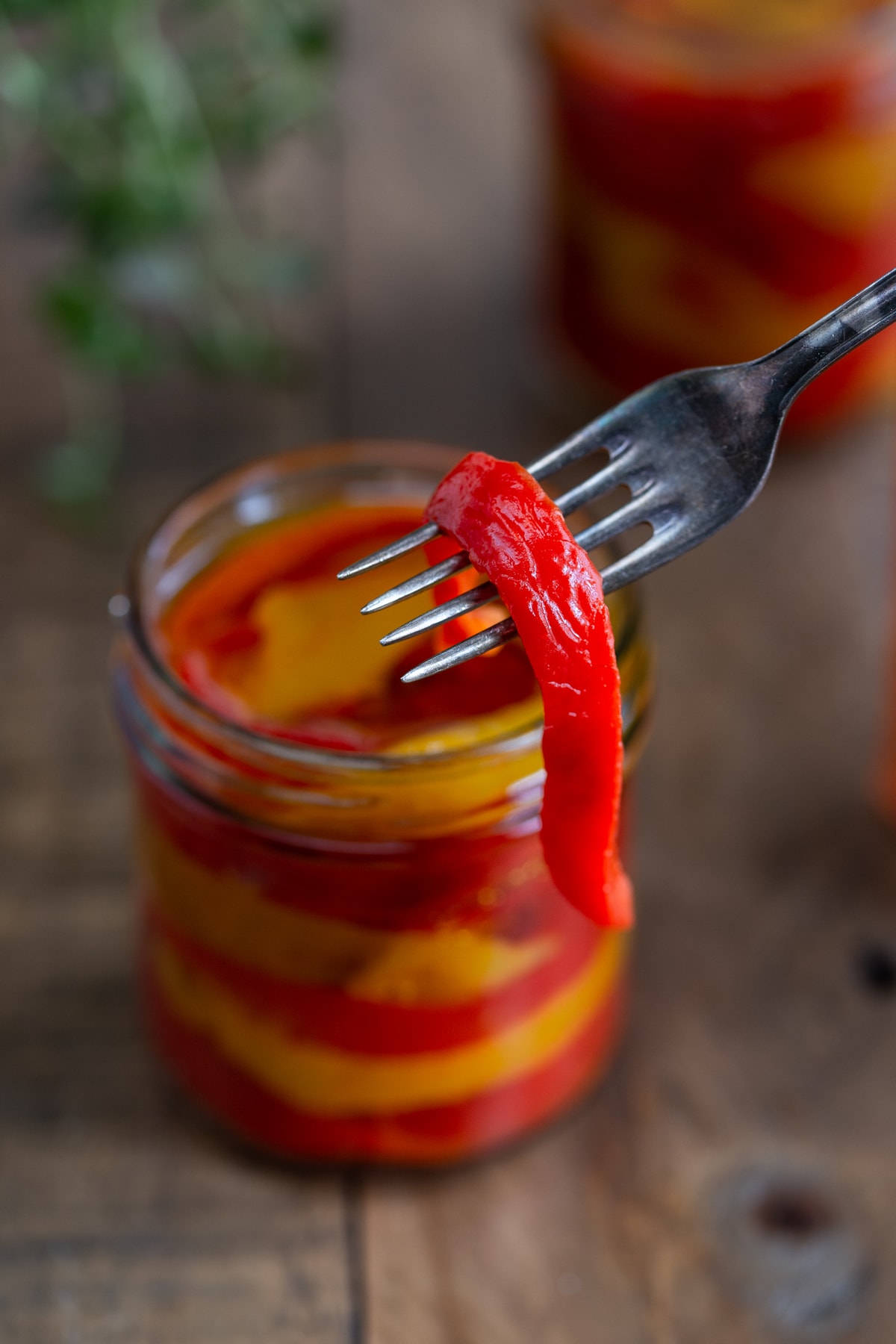 Oven-roasted bell pepper slice on fork, jars in the background.
