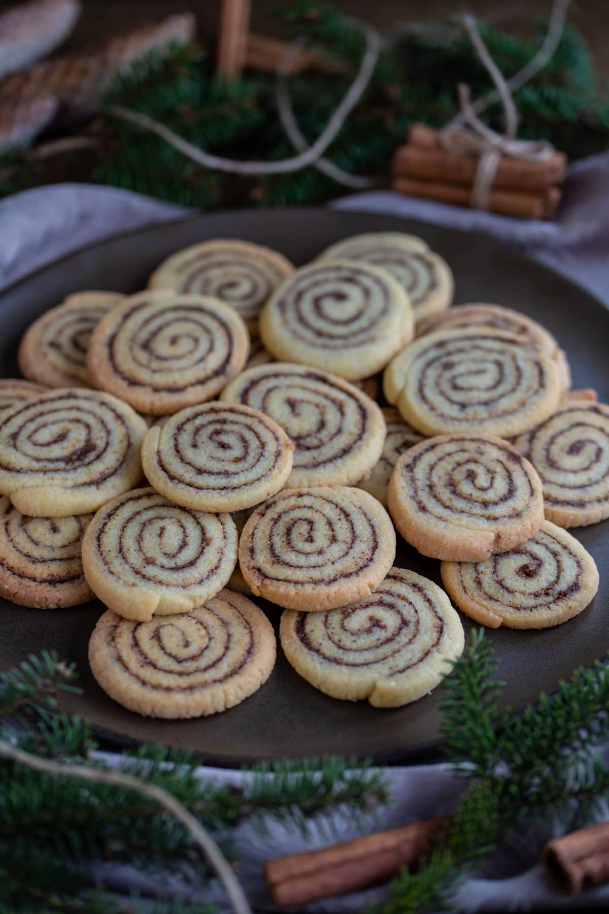 Kanelbulle cookies on a brown plate with pine decorations.