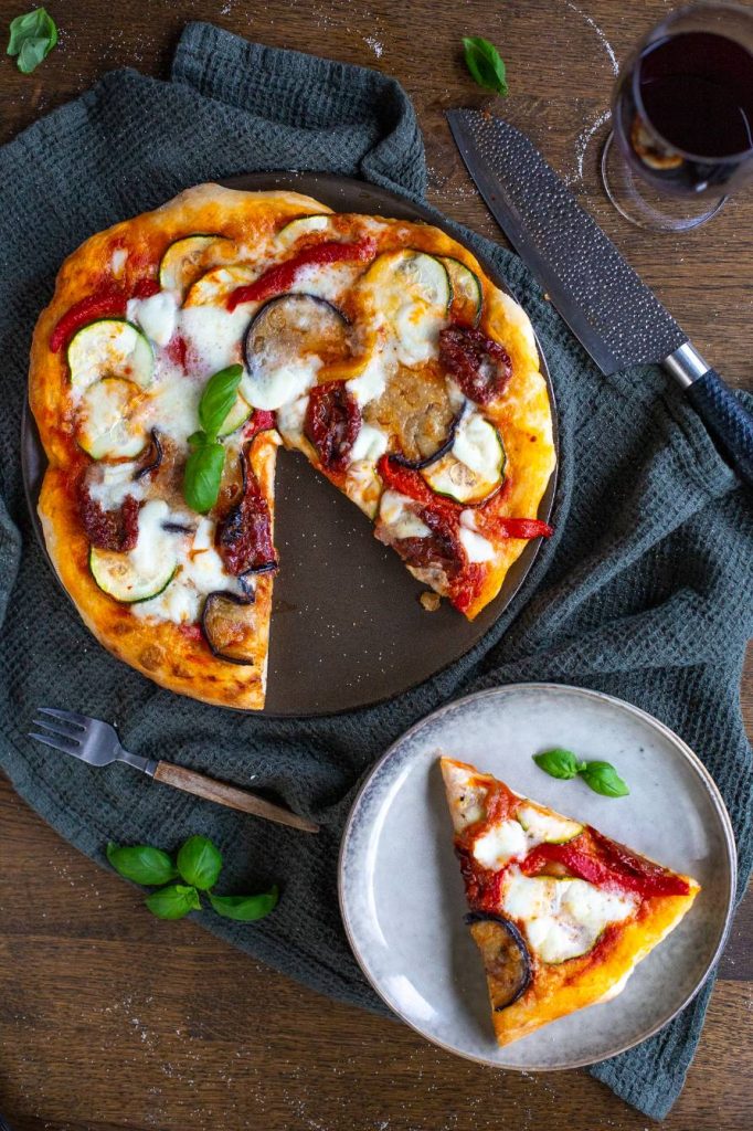 A vegetarian pizza slice on a small plate next to the rest of the pizza.