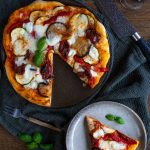 A vegetarian pizza slice on a small plate next to the rest of the pizza.