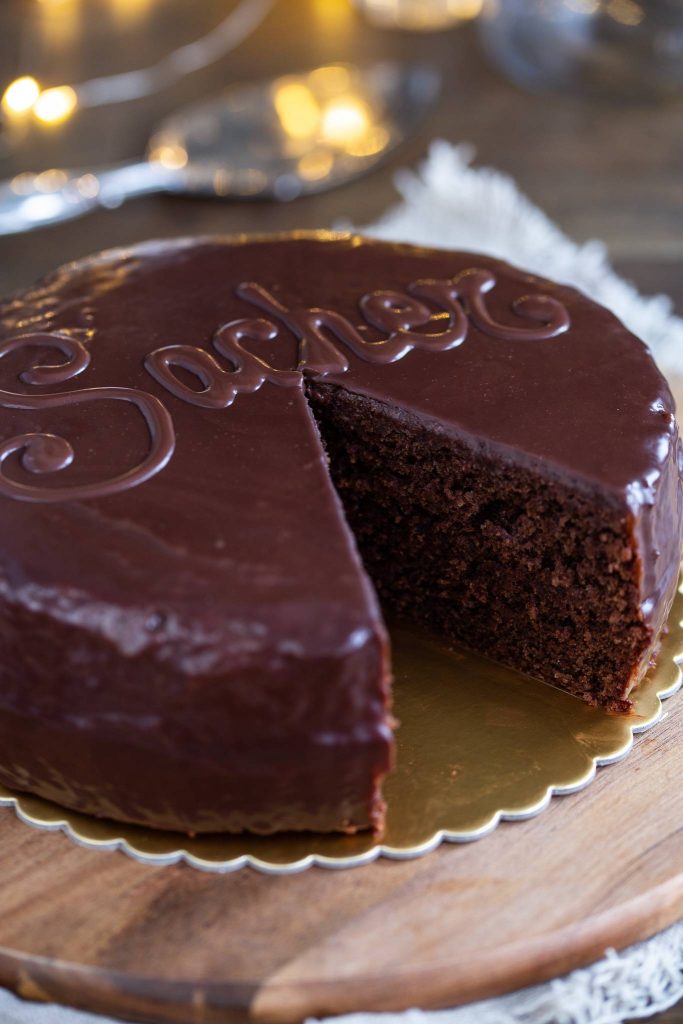 Sachertorte covered in ganache showing the classic "Sacher" decorative writing on top, with a slice removed.