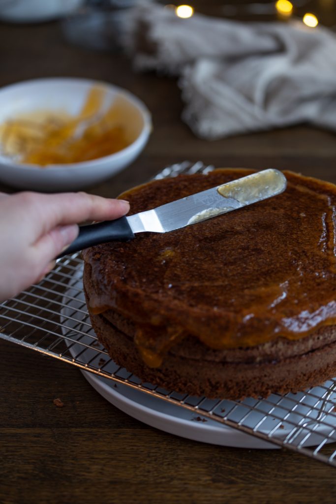 Spreading more apricot jam all over the assembled cake.