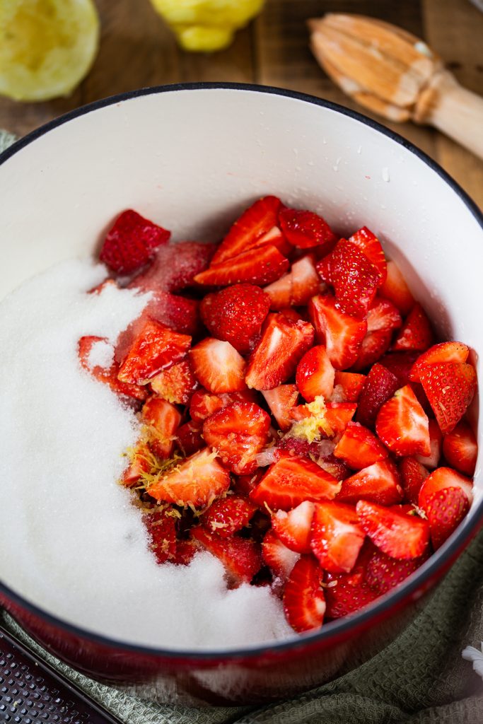 Sugar and lemon zest added to strawberries in a colander.