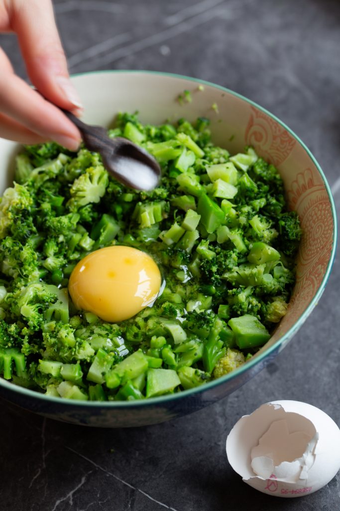 Sprinkling salt over broccoli and egg in a bowl.