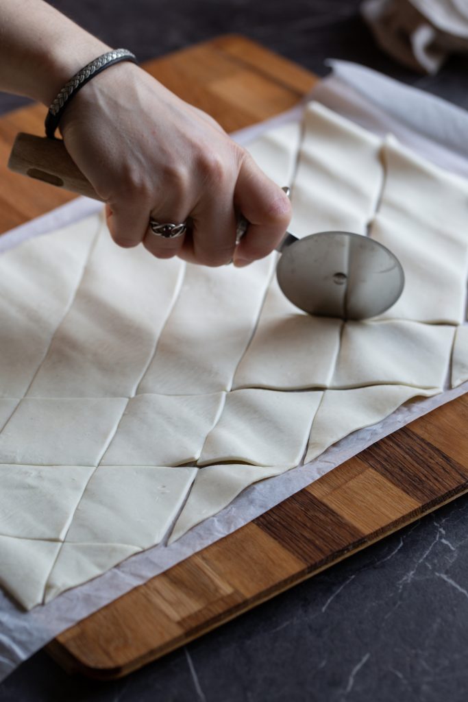 Hand cutting puff pastry sheet with pizza cutter.