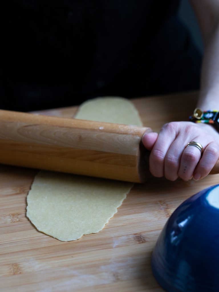 Flattening pasta dough with a rolling pin.