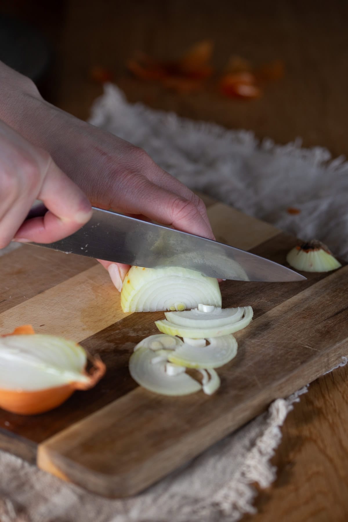 Hands with knife slicing yellow onion on a wooden cutting board.