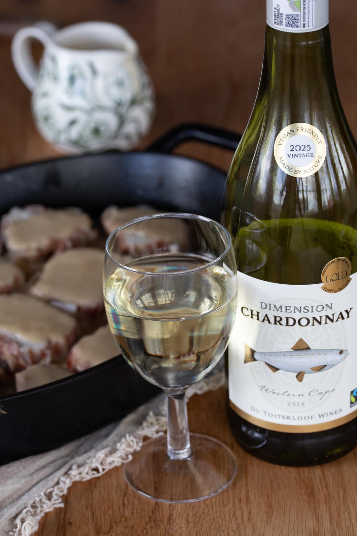 Glass and bottle of white wine in front of meat dish.