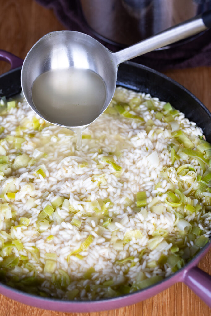 Ladle adding broth to risotto rice.