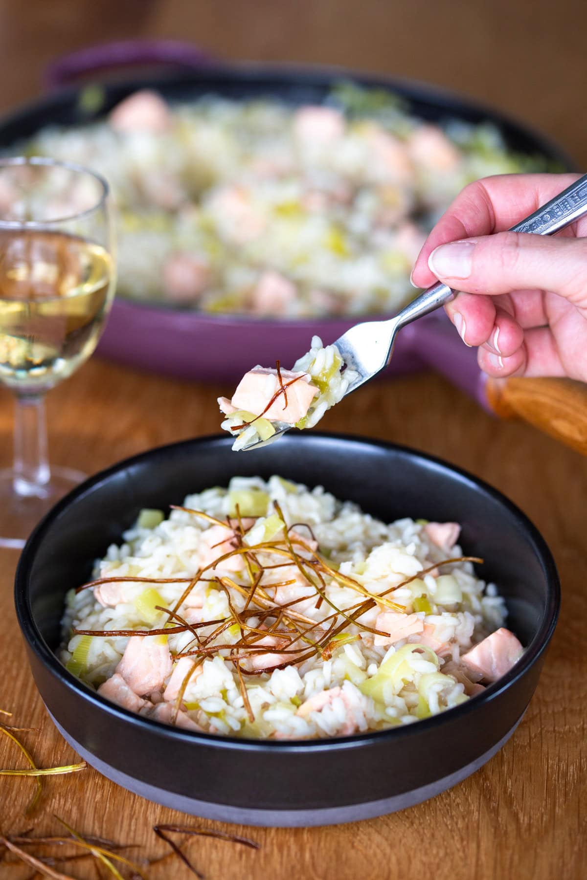 Salmon risotto topped with fried leek, fork lifting a small portion.