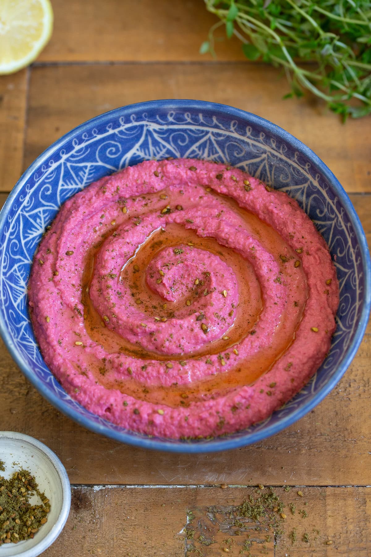 Vibrant pink beetroot hummus in a decorative blue bowl with herbs and lemon.