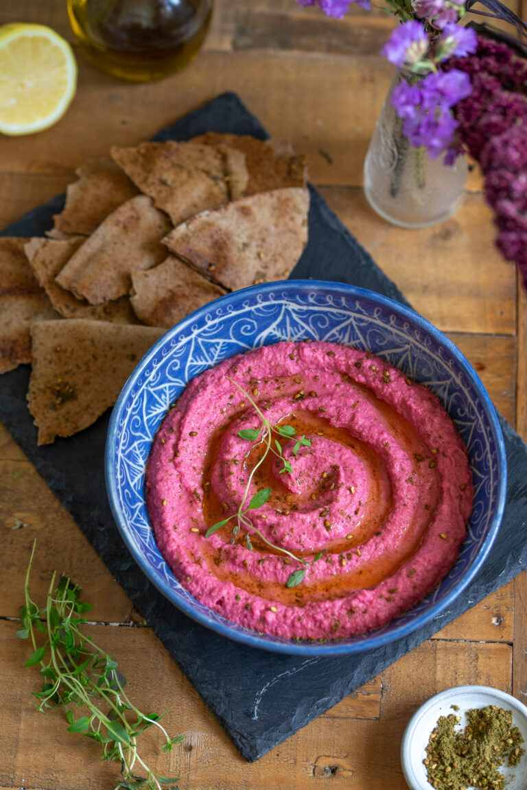 Beet hummus served in a blue bowl with pita bread chips.